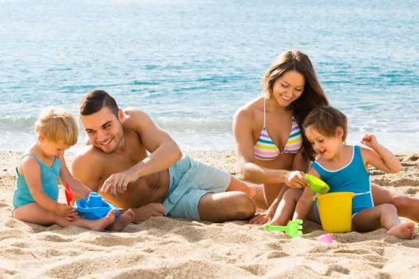 Happy smiling family of four playing with sand at beach in sunny day